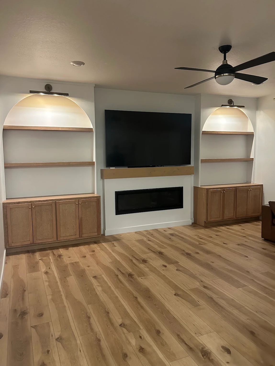 Custom built-in media wall with arched shelving, cabinetry and linear fireplace